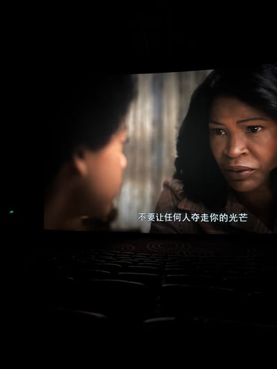 A still image shows two people facing each other. The person on top has brown skin, dark hair, and is looking down at the other person. Chinese text is superimposed over the image. The setting appears to be indoors, as there is a textured wall or object to the right of the people. The lighting is dim. The context includes the city of Taihe District, China.