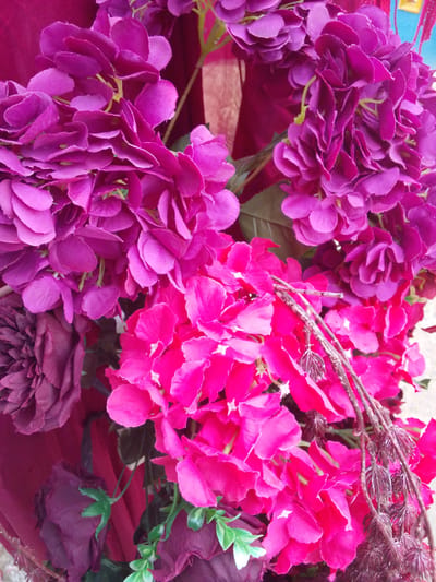 A close-up shot showcases artificial flowers, predominantly in shades of deep purple and bright pink. The flowers are densely packed together, creating a visually rich texture. Some stems and foliage are visible, adding depth to the arrangement. The scene appears to be indoors, perhaps in a decorative setting, possibly in Gampongjawa, Indonesia. No people or specific locations are discernible within the frame.