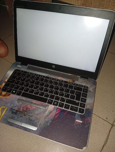 An open laptop displays a blank white screen. The device features an HP logo on the keyboard panel and "Bang & Olufsen" above. The keyboard itself is a standard QWERTY layout with black keys. A decorative, sparkling skin covers the lower half of the laptop, extending from the trackpad area down to the edges. The background is a tiled surface.