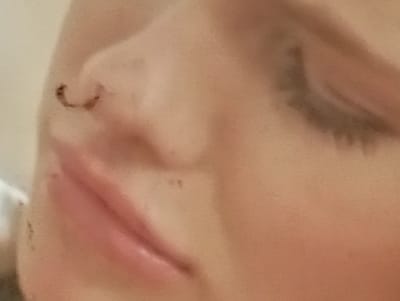 This is a close-up, slightly blurry, and cropped image focusing on the nose and lips of a person. The person appears to have a septum piercing, visible as a small hoop in the nostril. Their lips are painted with a pinkish-red lipstick, and the skin is a light to medium tone. The lighting suggests it might be indoors, with soft, diffused light. There are no visible text elements, and the image does not provide any specific cues about the time of day, weather, or emotional state. The context provided is Sofiivska Borshchahivka, Ukraine, but this information cannot be visually confirmed from the image itself.