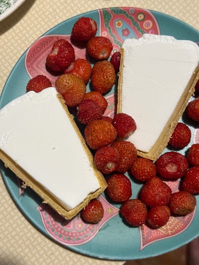 The image shows a close-up of a teal-colored plate filled with fresh strawberries and two slices of ice cream tarts. The tarts have a golden-brown crust and are filled with a white, creamy substance, likely ice cream or a similar frozen dessert. The strawberries are scattered around the tarts, some whole and some with small bites taken out of them, suggesting they are being eaten.
The plate has a decorative pattern with pink and light blue geometric shapes and floral motifs. The background appears to be a light-colored, textured tablecloth. The lighting suggests it might be daytime, possibly indoors, given the diffuse light and lack of harsh shadows. The overall scene conveys a sense of a casual dessert offering, possibly a snack or a light dessert after a meal. There are no people visible in the image, and no text is present. The presence of fresh strawberries and a sweet dessert hints at a pleasant, perhaps summery, occasion. Given the location context of Biysk, Russia, this could be enjoyed during the warmer months when strawberries are in season.