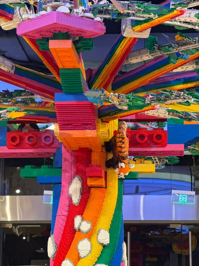 The image shows a Lego art installation featuring a colorful rainbow and a red panda. The installation is inside a building with a window. The location is Jinjiang District, China.