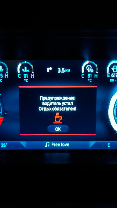 The image shows a digital display in a vehicle, likely a car's dashboard. In the center, a warning message in Russian reads "Warning: The driver is tired. Rest is mandatory!" Below the text is an icon of a steaming coffee cup and a button labeled "OK".
The surrounding display shows various car information:
- To the left, a temperature reading of "35 H" and "C".
- To the right of the warning, a distance of "3.5 KM" is displayed, indicated by a right-turn arrow.
- Further to the right, there are two gauges with readings "C 91 H °C" and "E 617 KM -".
- At the bottom left, a temperature of "25°" is visible.
- At the bottom center, a musical note icon precedes the text "Free love".
- On the far right, the letter "C" is partially visible.
The overall scene is dark, suggesting it's nighttime or the vehicle's interior is dimly lit, with the illuminated dashboard being the primary light source. There are no people visible in the image. The context of "Don Sak, Thailand" is not visually represented in the image itself and cannot be inferred from the provided visual data.