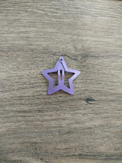 A single purple star-shaped hair clip rests on a wooden surface. The clip is centered in the frame and is lying flat. The wooden surface has a visible grain pattern and appears to be a light to medium brown color. There are no people or other objects visible in the image. The location in Крывасельскі сельскі Савет, Belarus is not determinable from the visual information presented.
