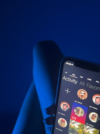 The image shows a close-up of a smartphone screen displaying an app called "Activity All Favorites". The screen features several circular profile icons labeled "new nenory". The phone is being held, and there is a blue light cast on the phone and the hand holding it, as well as on the background. The time displayed on the phone's status bar is 00:39. The photo's location in the city of Heenatigala Junction, Sri Lanka is not determinable from this image.