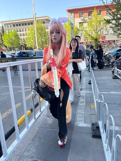 The image depicts a young person in cosplay, posing on a city street in Linghe, China. She wears a pink wig with bunny ears, an orange and white patterned costume, and black leggings. In her hands, she holds a closed, red-and-white umbrella, and a black purse with a white, stuffed mouse attached. Behind her, a man and a woman stand on the sidewalk. The backdrop includes buildings, parked motorcycles and bicycles, a white metal railing, and a street with parked cars. The image contains storefront signs with Chinese characters.