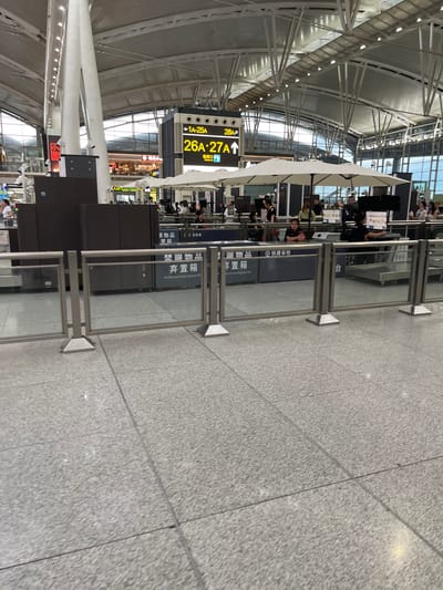 This media file depicts an interior scene within what appears to be a train station or airport in Panyu District, China. The primary subjects are people, a prominent digital signage system, and security checkpoints. The scene is brightly lit, suggesting it is daytime.
The digital signage displays flight or train information, with numbers like "1A-25A," "28A," and "26A-27A" indicating specific gates or platforms. Text in both English and Chinese is visible, including "Check in" and "铁路安检" (Railway Security Check). There are also signs indicating "Prohibited Article Disposal Bin," suggesting security procedures are in place.
People are observed at the security checkpoints, with some appearing to be in line or interacting with staff. The setting features a modern architectural style with high ceilings, exposed metal structures, and a tiled floor. Glass barriers are used to delineate queues for the security checks. While emotions are not explicitly discernible, the general atmosphere appears to be one of organized transit activity. The overall impression is a busy transportation hub.