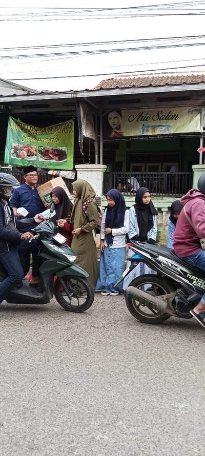 The image shows a street scene in Cangkuang, Indonesia, located at latitude -7.065 and longitude 107.552. The scene depicts a group of people standing and interacting in front of a shop. A man is wearing a black shirt and a black skullcap and is holding a small box. He is standing next to a man with a blue shirt and is holding a white paper bag in his left hand. Behind them is a dark green Honda motorbike and a man is driving it, wearing a blue shirt and black helmet. There is another motorcycle parked next to the Honda motorbike. Behind the Honda motorbike is a woman in a long green gown. Behind her is a woman in a light blue shirt and a long blue skirt. Behind her is a woman in a black hijab and a black shirt, and a woman in a black hijab and a white shirt. The woman in a black hijab and black shirt is looking to her left, and the other woman is looking to the right. The woman in a black hijab and a white shirt is holding a brown bag on her right shoulder. There is another woman in a grey shirt and a black hijab. There is a sign on the wall that says "Arie Salon." The sign is in Indonesian, which is the official language of Indonesia. There is another sign in Indonesian. The street is paved with concrete. There are power lines in the sky above the buildings. There are a few palm trees in the background. There is a large metal gate behind the people in the scene. The day is overcast, with the sky a light grey.