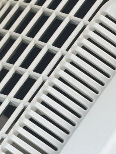 The image is a close-up, abstract shot of a white plastic grate with a dark background visible through its openings. The grate is composed of interlocking rectangular and slatted sections. The lighting creates shadows that highlight the texture and depth of the grate. There is no discernible location in the city of Kfar Saba, Israel, or any people or actions depicted.