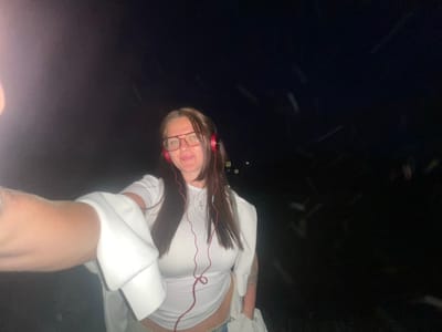 The image depicts a woman with long brown hair, wearing red headphones and glasses, and a white sweatshirt. She is oriented upside down in the frame, with a dark background suggesting a night setting. The location is potentially the city of Molokovo, Russia.
