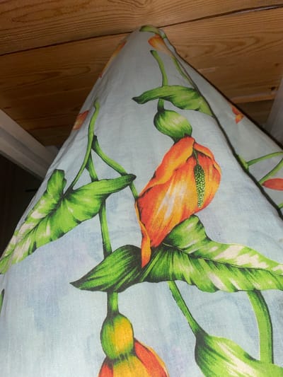 The image shows a light blue fabric with a floral print of orange and green flowers. The fabric is draped over what appears to be a wooden surface, possibly a ceiling or the underside of a structure. The lighting suggests an indoor environment, and the overall impression is of a close-up shot of a decorative item or material. There are no people or animals visible in the image. The specific location within Afanasyevo, Russia, cannot be determined from the visual information provided.