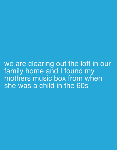 The image displays white sans-serif text against a solid cyan-blue background. The text describes an event taking place within a residential property in Wealden, United Kingdom. An individual, referred to as "I," along with others identified as "we," are engaged in the action of clearing out the loft of their family home. During this activity, the individual "I" discovered a specific object: a music box. This music box is explicitly identified as belonging to the individual's mother, originating from her childhood in the 1960s. The scene implies the presence of multiple people undertaking the task of organizing or removing items from an attic space within a private dwelling.