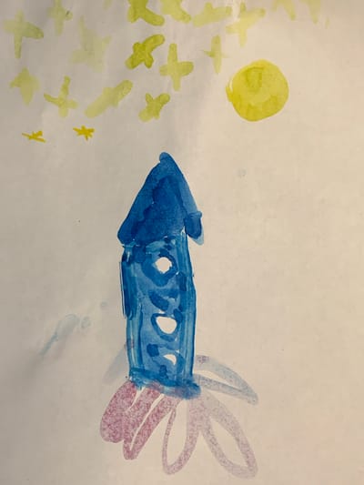 A watercolor painting depicts a childlike drawing of a blue rocket ship flying through space. The rocket is elongated with a pointed nose and has circular windows along its body. It has pink and blue fins at the rear, which are smudged and blended. To the left of the rocket, a yellow circle represents the sun or a planet, surrounded by several yellow, star-like shapes. A few small yellow asterisks are also scattered in the scene. The overall impression is a simple, whimsical depiction of space travel, created with loose brushstrokes and vibrant colors. The background is a light, textured white, suggesting paper.
