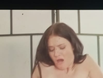 The image shows a close-up of a woman's face and upper torso, with her eyes closed and mouth open. She has dark hair and appears to be in an intimate setting. The background is a light-colored, segmented wall, possibly a room divider or screen. There is a black border at the top of the image. There is no information in the image to suggest the location is Sofiivska Borshchahivka, Ukraine.