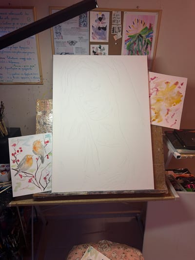 This media file captures an artist's studio space, filled with canvases and art supplies. The central focus is a large, blank canvas on an easel, lightly sketched with what appears to be a flowing, abstract design. To the left of the main canvas, pinned to a corkboard, are several smaller pieces of artwork and what seem to be inspirational notes or statements. One note reads "I AM MY OWN MUSE" in bold letters. Below this, another pinned document contains text in Bulgarian, discussing artistic vision, values, and focus.

To the right of the main canvas, a smaller, finished watercolor painting depicts two robins perched on a branch adorned with red berries. Another abstract watercolor painting with yellow and pink tones is positioned above the main canvas. Various art supplies, including brushes and paint tubes, are visible on shelves and in a jar in the foreground, indicating active artistic work. The overall impression is one of a creative and organized workspace, likely in a home studio. The lighting suggests it might be daytime, with artificial light sources also contributing to the scene. The Bulgarian text suggests the location context of Svilengrad, Bulgaria.