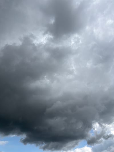 The media file shows a dramatic sky filled with dark, heavy storm clouds. The clouds are predominantly a deep gray, with some areas appearing almost black, suggesting an impending downpour. Lighter, more wispy clouds are visible in the upper right quadrant, where patches of bright blue sky can be seen peeking through, hinting at a break in the storm or a transition in the weather. The lighting suggests it might be late afternoon or early evening, as the sunlight is filtered through the dense cloud cover, creating a somber and intense atmosphere. There are no people or man-made objects visible, focusing solely on the natural phenomenon of the stormy sky. The overall impression is one of powerful natural forces at play, evoking a sense of awe or anticipation of the weather to come. The location context of Męcina, Poland, places this scene in a specific geographical setting, though there are no visible landmarks to confirm this visually within the image itself. The image is a photograph taken from below, looking up at the sky.