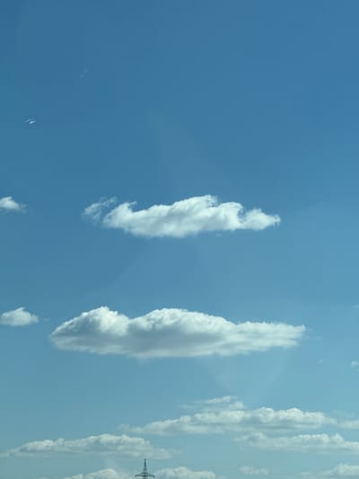 The image depicts a daytime sky in Hegyeshalom, Hungary. The sky is predominantly blue with scattered clouds. On the right side of the frame, there are multiple vertical cloud formations. Towards the bottom right, a power line tower can be seen.