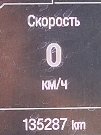The image displays a digital vehicle dashboard interface, specifically showing primary operational data. The top section features the Russian word "Скорость" (Speed) in white pixelated text. Below this, a large digital "0" indicates the current speed, followed by "КМ/Ч" (KM/H), confirming the vehicle is stationary. A horizontal white line separates this information from the odometer reading at the bottom, which displays "135287 km," indicating the total distance traveled by the vehicle. The screen background is a dark, mottled grey. No individuals or external environmental details are visible. This scene is reported to be located in Hiyaban, Uzbekistan.