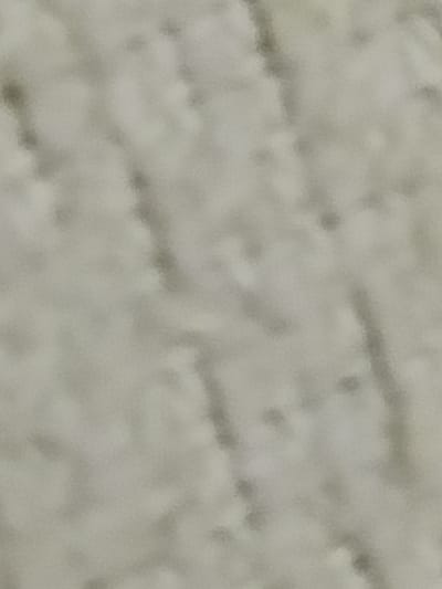 The image is a close-up, abstract view of a textured surface. The surface appears to be light-colored, possibly white or a very pale gray, with darker, irregular lines and patches creating a mottled or patterned effect. The texture is soft and slightly fuzzy, suggesting it might be fabric, a rough plaster, or a similar material. There are no discernible objects, people, or activities visible. The lighting is diffuse, creating soft shadows and highlights across the surface. The image lacks any contextual clues to indicate a specific location within Al Hadaba, Egypt.