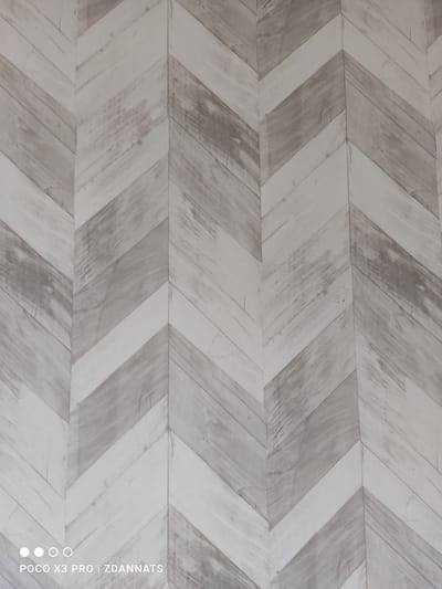 The image displays a close-up of a wall with a herringbone pattern, resembling distressed wooden planks. The pattern consists of alternating light and dark gray diagonal lines, creating a chevron or herringbone effect. The texture appears to be that of aged wood with visible grain and some subtle variations in color and shading, giving it a rustic and weathered look. There are no people or specific objects visible within the frame, and the environment is solely the patterned wall. The bottom left corner of the image shows a watermark with "POCO X3 PRO | ZDANNATS". This image does not contain any information that would allow for the identification of its location in Vologda, Russia, or any other specific geographical area.
