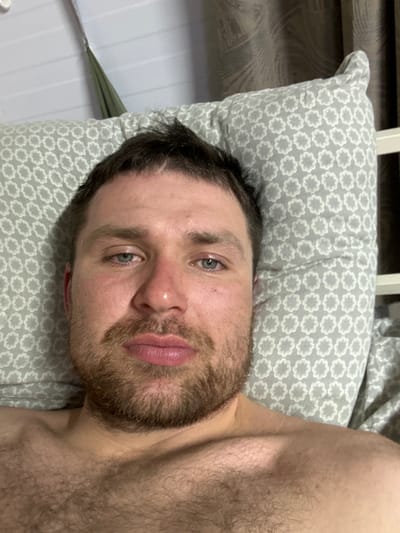 A Caucasian male with a beard and short, dark hair is lying on a pillow with a gray and white floral pattern. He appears to be resting in a supine position. His chest and upper torso are visible, suggesting he is shirtless. The background shows part of a white bed frame. There is no visual evidence to indicate this image was taken in Nizhnekamsk, Russia.