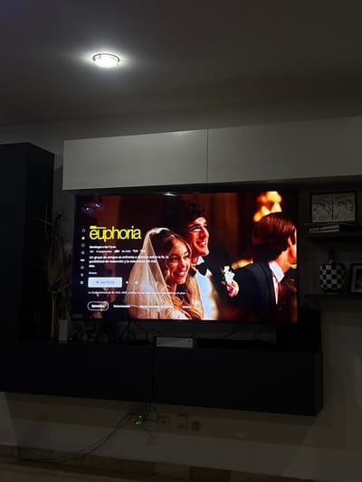 The image shows a television displaying the title screen for the HBO show "Euphoria." The screen features a man and woman smiling and looking at each other, dressed in what appears to be wedding attire. The television is mounted on a wall unit that is partially white and black. Various items are on shelves above the television. The setting appears to be indoors. The precise location of Santa Clara Ocoyucan, Mexico, is not discernible in the image.