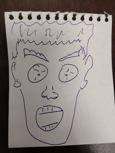 The image is a blue ink drawing on a torn sheet of lined paper. The drawing depicts a caricature of a face with wide, shocked eyes, a prominent nose, and an open mouth with visible teeth. The hair is drawn with a jagged, wavy line. The paper appears to be a page torn from a spiral-bound notebook, indicated by the perforated edge at the top. The background is a dark, textured surface, likely a wooden table. There are no people or animals present in the image, and no specific details suggest a location in Novosaratovka, Russia.