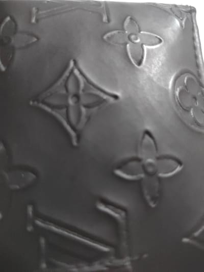The image is a close-up, slightly blurry shot of a dark-colored object with an embossed pattern. The pattern appears to be a repeating floral or geometric design, characteristic of luxury brand monograms. The texture of the object seems to be matte with some subtle sheen due to lighting. The background is indistinct, but the overall impression is of a detailed, textured surface. There is no indication of the city of Dorkovo, Bulgaria, or any other specific location within the provided image. The description is limited to the visual elements present in the photograph.