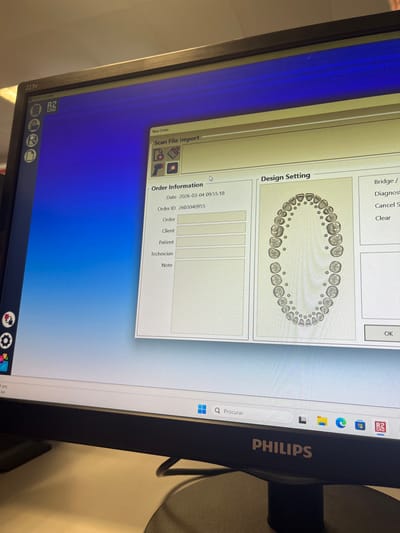 The scene is a close-up, angled view of a Philips 223V computer monitor displaying a dental software application, located in Gandra, Portugal. The monitor shows a "New Order" window with a blue gradient background. Within this window, there are sections for "Scan File Import" and "Order Information," which lists the Date as "2026-03-04 09:55:18" and the Order ID as "2603040955." Below these, fields for "Order," "Client," "Patient," "Technician," and "Note" are visible but unpopulated. To the right, a "Design Setting" panel displays a detailed anatomical diagram of a full human dentition, showing both upper and lower arches with individual teeth. Partially visible on the far right are sections labeled "Bridge /" and "Diagnosis," along with "Cancel S," "Clear," and "OK" buttons. The bottom of the monitor reveals a portion of the Windows 11 taskbar, including the "Procurar" (search) bar and several application icons. The monitor rests on a dark, circular base, with a cable visible behind it. No individuals are present in the image. The immediate environment appears to be an indoor setting, likely an office or laboratory, with a light-colored surface visible in the upper background.