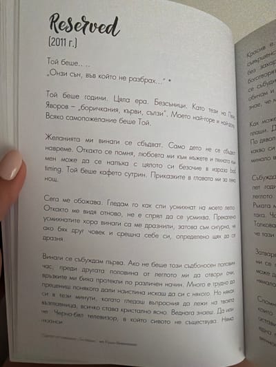 The image shows an open book with text in Bulgarian. The left page has a large cursive title "Reserved" followed by "(2011 г.)" in parentheses. Below this, there are several paragraphs of text. The right page also contains text, but it is partially obscured and appears to be in a smaller font size. The book is lying flat, and a person's hand with manicured nails is visible on the left side of the left page. The background is out of focus, suggesting a soft, indoor environment. There is no information in the image that links it to the city of Pazardzhik, Bulgaria.