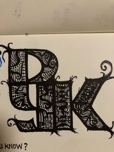The image shows a close-up of a black ink drawing on a white page, likely from a sketchbook, with faint pencil markings visible on the left page. The drawing features an ornate, gothic-style letter or symbol, heavily decorated with intricate patterns and fill. The main subject is this stylized letter, which appears to be composed of multiple interconnected sections. The top portion has a pointed, almost crown-like shape with a spiral flourish at the top left. Below this, a rectangular section is filled with dense, abstract patterns. The largest part of the drawing is a curved form, reminiscent of a stylized 'P' or a crescent moon shape, also filled with detailed patterns. Another smaller, jagged section extends to the right.
The patterns within the letter include parallel lines, wavy lines, dots, and eye-like shapes, giving it a textured and complex appearance. The drawing style is characterized by bold black lines and fine detail.
To the right of the drawing, oriented vertically, is the text "LL KNOW?". The pencil markings on the left page are illegible, but appear to be notes or doodles. The lighting suggests an indoor setting, and the focus is entirely on the artwork and the immediate surrounding page. The overall mood is artistic and focused on intricate design. There are no clear indications of a specific time of day, weather, or strong emotions conveyed by the artwork itself. The location context of Sabadell, Spain, is noted but not visually represented in the image.