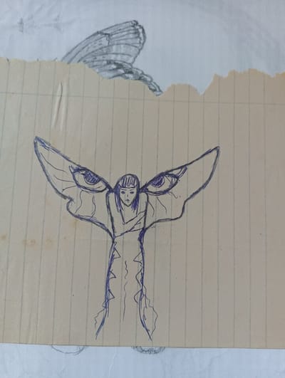 A pen drawing on lined paper depicts a figure with human-like features. It has a female face with short hair. The figure is slender, with arms crossed over its chest. Its wings resemble insect wings with large eyes depicted on each. The paper on which it is drawn is torn and partially covers another drawing of a butterfly wing. The image gives no indication of location in Karnobat, Bulgaria.