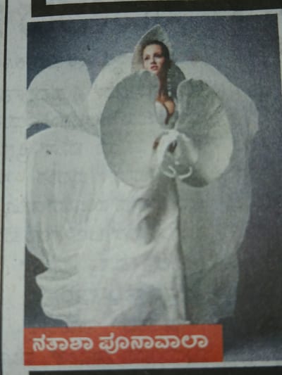 A newspaper clipping featuring a woman in a white gown positioned within the form of a flower. The text on a red bar to the right is written in Kannada script. The location is Bengaluru, India, as indicated by the Kannada script used in the text.