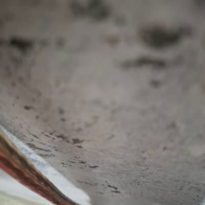 The image is a close-up, low-angle shot of a textured, light-colored surface with darker speckling. The surface appears to be slightly curved, with a metallic or reflective object in the lower left corner. The speckling suggests a mottled or stained appearance. The background is out of focus, showing a continuation of the textured surface. There are no people or discernible structures present in the image. The location in the city of Reudeuep, Indonesia, cannot be determined from the visual information provided.