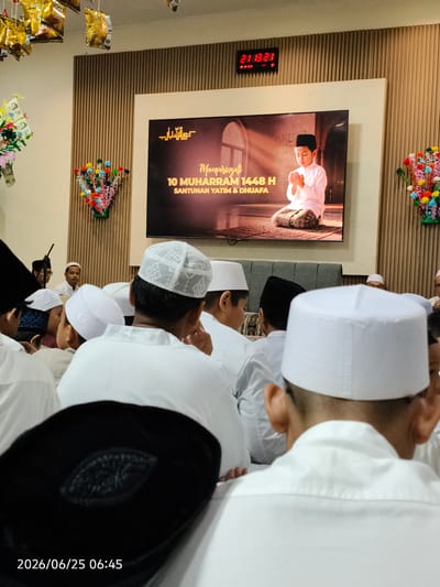 This media file depicts an indoor scene with a group of young boys and men, likely at a religious gathering or ceremony. The primary subjects are the individuals, most of whom are wearing white peci caps, a traditional Indonesian Islamic cap, and white attire, suggesting a formal or religious occasion. One prominent object is a large digital screen displaying an image of a young boy praying, with Arabic text and "Memperingati 10 MUHARRAM 1448 H SANTUNAN YATIM & DHUFA" prominently featured. This indicates the event is commemorating the 10th of Muharram 1448 Hijriah, a significant date in the Islamic calendar, and involves the distribution of alms to orphans and the needy.

In the background, a digital clock shows "21:13:28", indicating the time is around 9:13 PM. The setting appears to be a well-lit room with wooden paneling on the walls. Decorative elements, such as colorful floral arrangements and what appear to be money bouquets (often used in Indonesian cultural celebrations), are visible, adding to the festive or commemorative atmosphere. The overall mood seems solemn yet communal. The visible text includes the time on the digital clock, the event details on the screen, and a timestamp at the bottom left corner of the image: "2026/06/25 06:45". The location context provided is Depok, Indonesia.