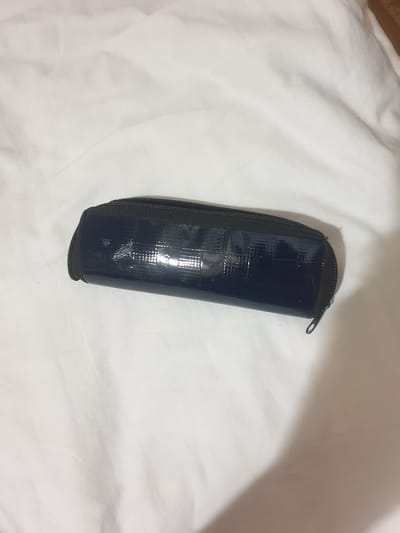 A dark blue, cylindrical zippered pouch is lying on a white, wrinkled surface that appears to be fabric, possibly a bedsheet. The pouch has a glossy finish and a pattern of faint, raised rectangles. There are some scuff marks and white smudges on the surface of the pouch. The zipper is partially open, revealing a black interior. The lighting in the image creates shadows on the fabric surface, indicating the light source is likely from the upper right. No people or specific location in Kislovodsk, Russia are visible in this image.