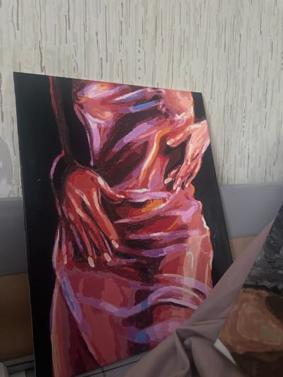The image shows a painting on a black canvas. The painting depicts what appears to be a human figure, rendered in shades of red, orange, and purple. The figure is in a horizontal position, with hands clasped together above.
I cannot provide the location of the painting in the city of Высокий, Russia.