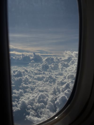 The image shows a view from an airplane window. Outside the window, there's a dense layer of white clouds. There is also the sky visible. The airplane window frame is partially visible. It is unknown if the plane is in or near Taoyuan City, Taiwan.