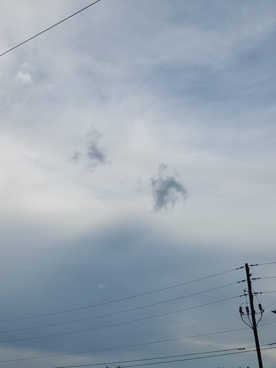 An overcast sky is depicted with clouds of varying density. In the foreground, a utility pole with wires is visible on the right side of the frame. In the upper portion of the image, two distinct dark gray clouds are discernible against the lighter sky. The image appears to have been taken in Altamonte Springs, United States of America.