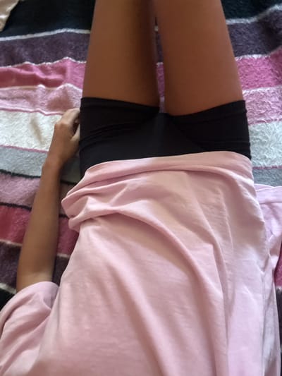 This media file is a close-up, top-down view of a person lying on a striped blanket. The person is wearing black shorts and a pink t-shirt. The blanket has stripes of pink, purple, and white. The person's right arm is visible, resting on the blanket. The scene appears to be indoors, with soft lighting. There is no visible text in the image. The overall impression is one of relaxation or rest.