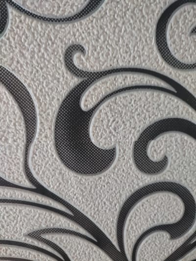 The image shows a close-up of a textured, light-colored surface with a repeating black and grey scroll pattern. The texture appears to be a raised, stippled effect. The pattern consists of swirling lines and curved shapes, some filled with a grey dotted pattern, and outlined in black. The lighting is even, with no harsh shadows, suggesting an indoor or overcast environment. There are no people, animals, or distinct objects visible beyond the patterned surface itself. The location in Narowlya, Belarus, is not discernible from the visual information in the image.