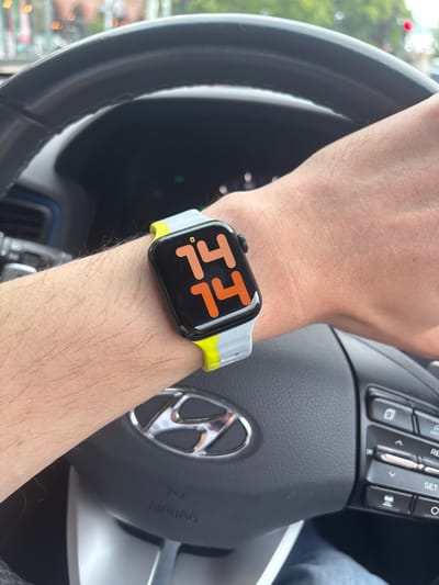 A person's arm is shown in the interior of a car, with an Apple Watch on the wrist. The watch face displays the time as 11:14 in orange numbers on a black background, and it has a two-tone grey and yellow band. The person's hand is resting on a black steering wheel featuring a silver Hyundai logo. The image was likely taken in daylight, though the precise location within Knutsford, United Kingdom is not discernible from the provided details.