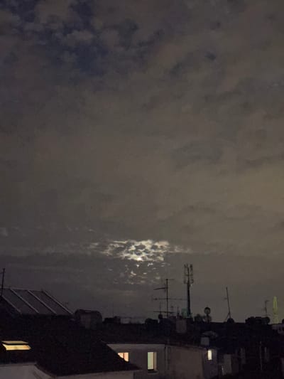 The image shows a nighttime view over the rooftops of Duisburg, Germany. A cloudy sky with patches of moonlight filters through. Several antennas and a cell tower are visible on the rooftops. The scene is dark, with some windows illuminated by interior lights.
