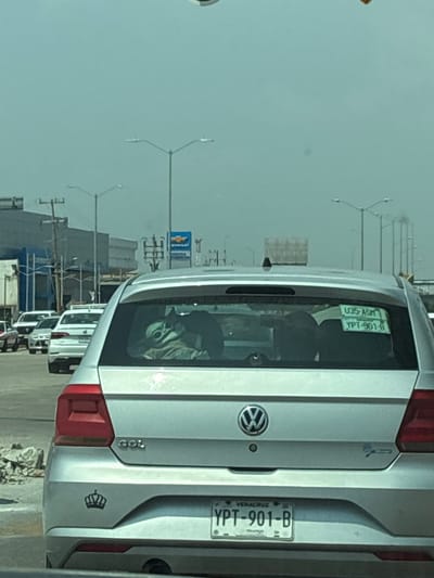 A slightly angled, medium shot depicts the rear of a silver Volkswagen Gol in a line of traffic on a paved road. The vehicle has a Veracruz license plate that reads "YPT-901-B" and a sticker on the rear window that reads "U35-ASM" and "YPT-901-8". A small crown-shaped emblem is visible on the rear bumper. In the background, streetlights, utility poles, and buildings are visible, including a Chevrolet dealership. The overall scene suggests an urban environment in Coatzacoalcos, Mexico.