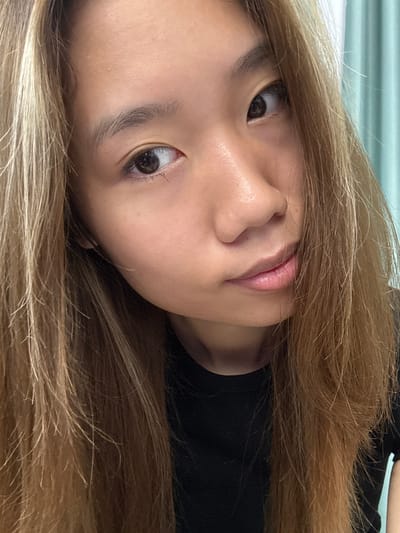 A close-up, angled portrait of a young woman with light brown hair. Her face is positioned slightly off-center, with her eyes open and directed toward the viewer. Her skin tone is fair, and her lips are slightly parted. She appears to be wearing a dark-colored top. The background is out of focus, suggesting a soft or diffused light. There is no indication of the location being in Nan'an District, China, as no contextual clues are present.