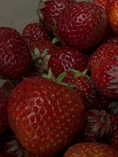 This media file showcases a close-up view of several ripe strawberries. The strawberries are a vibrant red, with visible seeds and some exhibiting slight blemishes, suggesting they are fresh and natural. The lighting is somewhat dim, which accentuates the rich color of the fruit and creates a soft, slightly blurred background. The image is tightly framed, focusing exclusively on the strawberries, with no other objects or surroundings visible. The shallow depth of field ensures that the strawberries are the primary subjects, with some appearing sharper than others, creating a sense of texture and dimension. There is no indication of people, activity, or a specific time of day or weather. The location context provided is Узюково, Russia, but there are no visual cues within the image to confirm this. No text is visible in the media file.