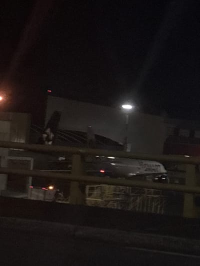 Captured at night in Rionegro, Colombia, the image shows an airplane partially visible against an illuminated structure. A street lamp is also visible. The image is grainy and dark.