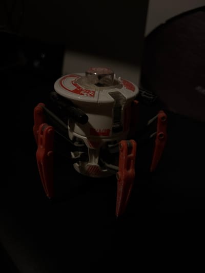 A close-up shot of a toy probe droid against a dark background. The droid is primarily white with red markings and orange appendages. The image appears to have been taken indoors with limited lighting. San Juan Cuautlancingo, Mexico is not evident in the image.