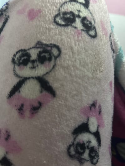 The image shows a close-up of a pink fuzzy fabric with a pattern of panda faces and pink bows. The pandas are primarily white with black markings around their eyes and ears. The pink bows are next to the pandas' heads. The fabric appears soft and plush. There is no information about the location, San Juan de Los Morros, Venezuela.