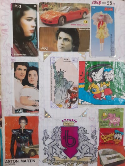 This media file appears to be a collage of various collectible items, possibly trading cards or stickers, arranged on a surface resembling notebook paper. The items depict a range of subjects, including people, cartoon characters, and objects.
One card features a doll with blonde hair and a yellow dress, accompanied by text in Russian and English: "My yellow flower" and "МОЙ ЖЕЛТЫЙ ЦВЕТОК". Another card displays a red sports car and a woman's face, with the name "Kassandra" and "HONDA MSX Km/h280" visible. There is also a card with a close-up of two people, labeled "Kassandra" and "ARI". Another card shows a woman in a futuristic outfit, identified as "ASTON MARTIN LAGONDA".
Cartoon characters are also present, including Donald Duck and characters from "Dany Bubble Gum". A depiction of the Statue of Liberty is on another card, with "U.S.A AMERICA" printed below it, and some Turkish text that seems to indicate a date and authorization. A drawing of a lion crest with a crown is also visible.
The overall arrangement suggests a personal collection or a scrapbook. The visible text indicates a mix of languages, including Russian, English, Turkish, and possibly Arabic or Persian script on the "Dany Bubble Gum" packaging. The numbers "1998-99" suggest a time frame for the collection. The context of Semey, Kazakhstan, is provided, but no specific location cues are apparent within the image itself to confirm this. The emotional tone is neutral, as the file focuses on the display of collectible items.